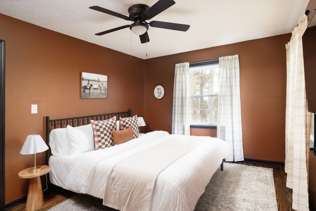 King bedroom with chestnut walls, warm wood floors, and two bright windows
