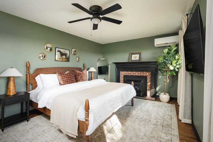 King bedroom with sage walls, horse artwork, a four-poster bed, and brick fireplace